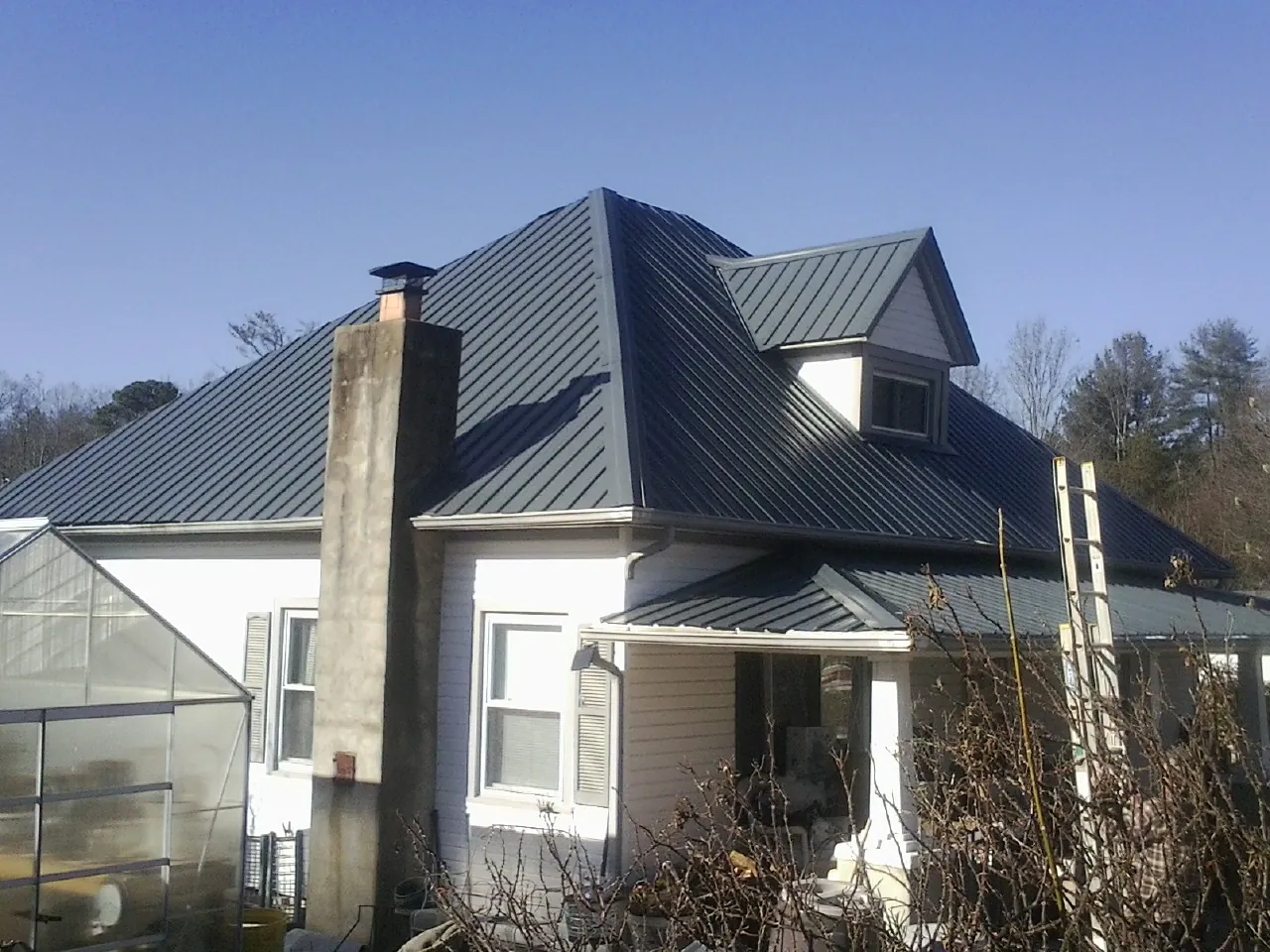 Dark blue standing seam metal roof on a white farmhouse with dormer — Slate & Tile Roof Repair by Roofing Brothers in Kelford