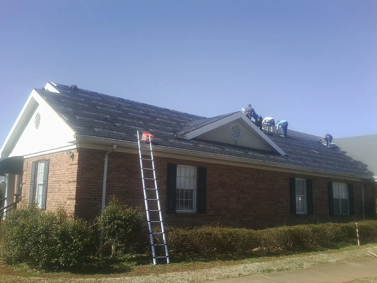 Crew tearing shingles off a brick ranch roof with a ladder set — Emergency Roof Repair work by our crew in Kelford