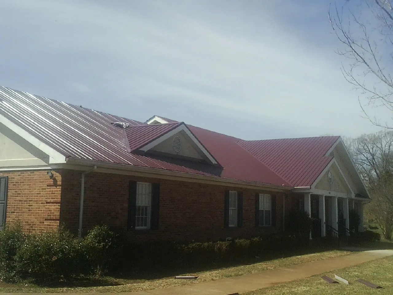 Red metal roof with gabled entries on a long brick building, from a Hail Damage Roof Repair job in Kelford