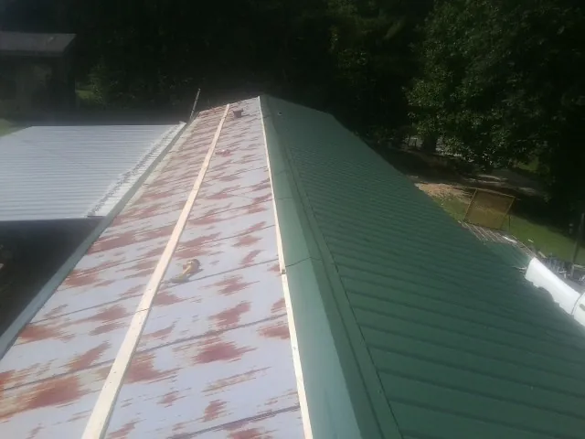 Old rusted panels beside newly installed green metal roofing — Wind Damage Roof Repair by Roofing Brothers in Kelford