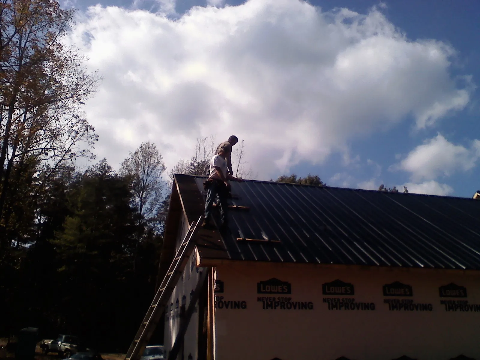 Roofer fastening dark metal panels high against a cloudy sky, from a Roof Inspection job in Kelford