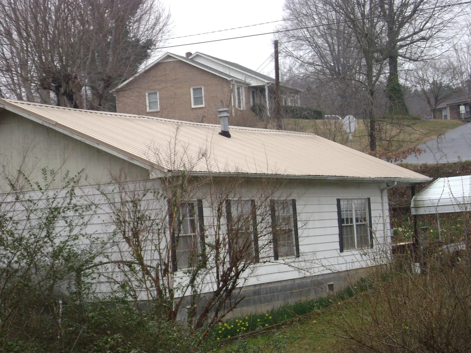 Tan metal roof on a white sided house set into a hillside — Commercial Roofing by Roofing Brothers in Kelford