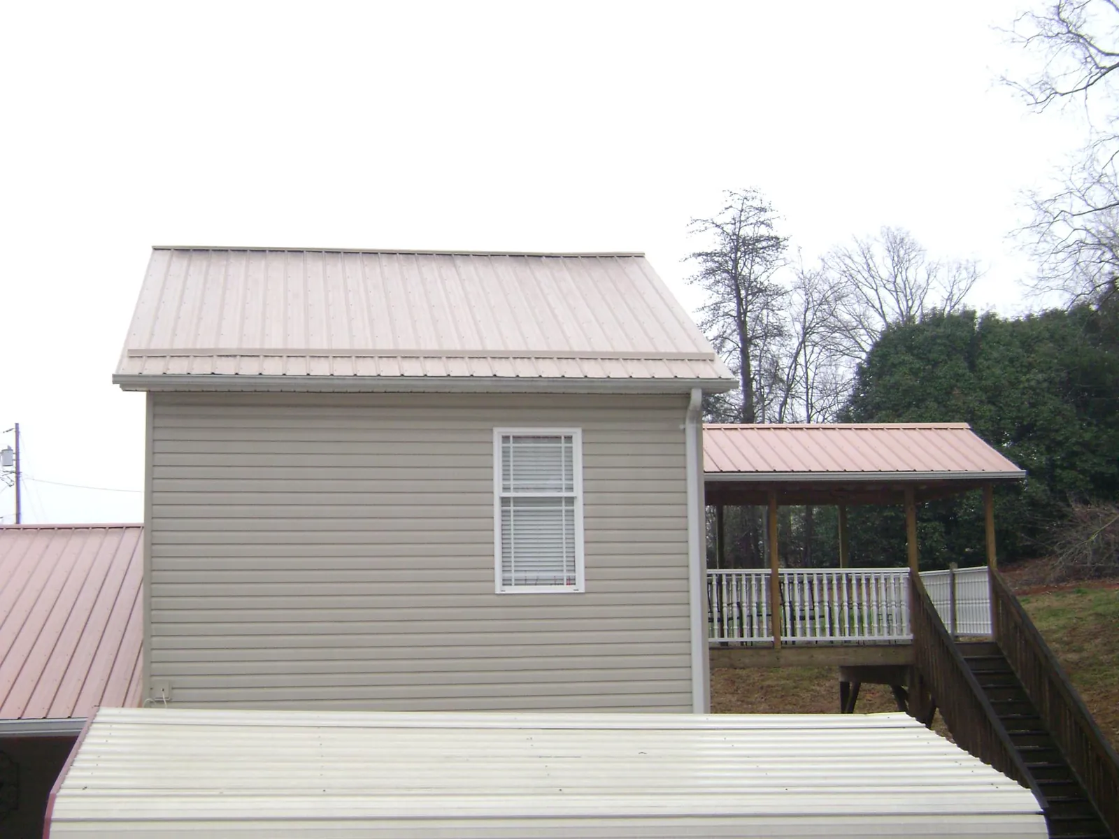 Tan metal roofs on a two story addition and attached porch, from a Roof Replacement job in Kelford